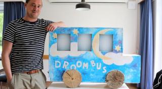 Benjamin van Jeugdzorg Emmaüs Mechelen poseert naast een maquette van de droombus